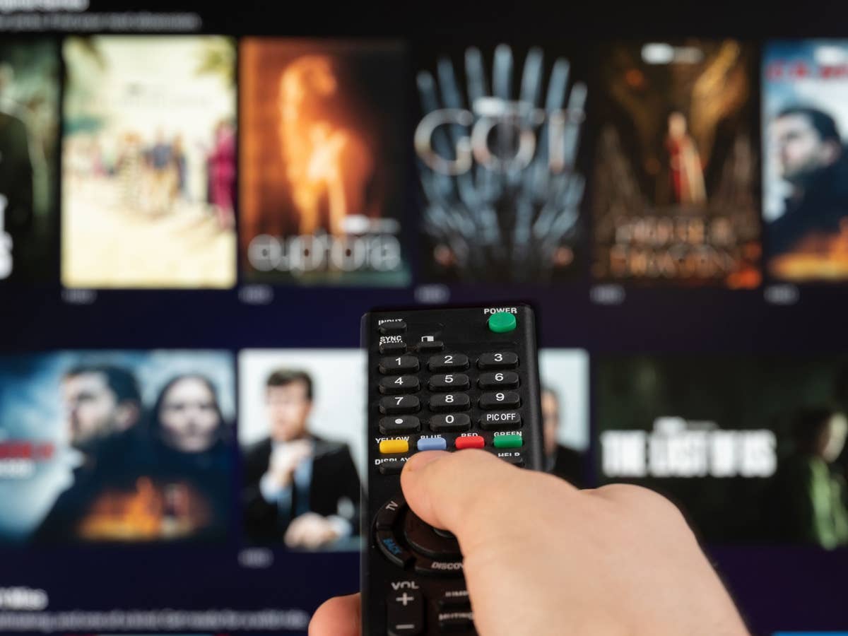 Person zeigt auf einen Fernseher auf dem verschiedene Serien und Filme zu sehen sind