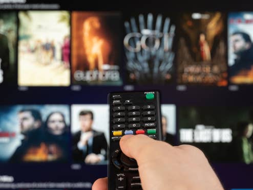 Person zeigt auf einen Fernseher auf dem verschiedene Serien und Filme zu sehen sind