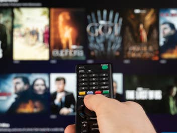 Person zeigt auf einen Fernseher auf dem verschiedene Serien und Filme zu sehen sind