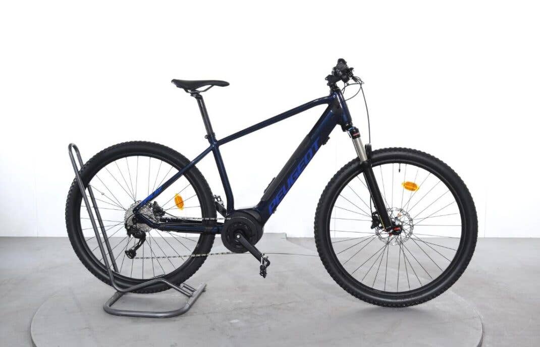 Schwarz-blaues E-Mountainbike von Peugeot steht vor einer weißen Wand