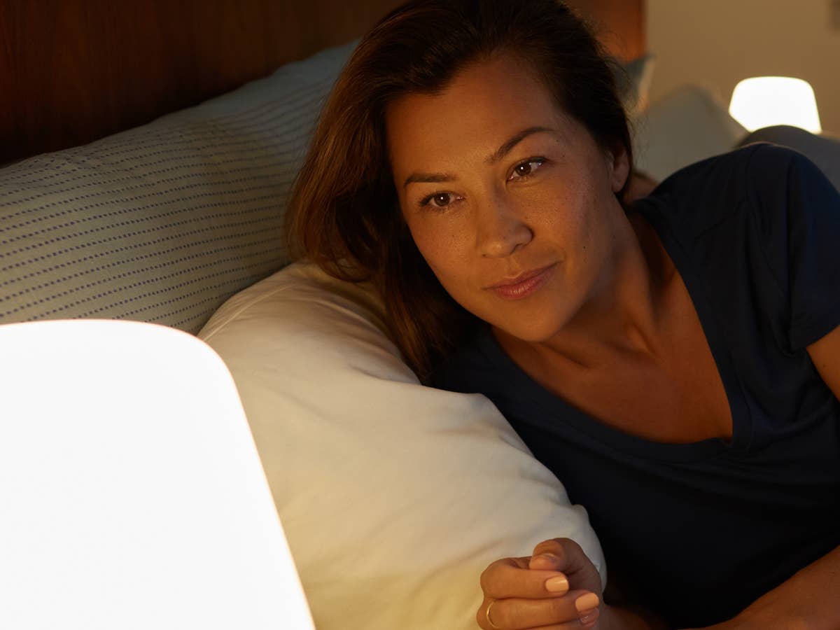 Frau im Bett schaut auf eine smarte Lampe