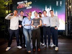 Sieben junge Erwachsene stehen lächelnd auf einer beleuchteten Bühne vor einer großen Leinwand mit der Aufschrift „ROAD TO MAILAND CORTINA 2026“ und halten ihre Auszeichnungen in den Händen.