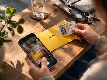 Eine Frau mit einem POSTIDENT-Umschlag, einem Smartphone und einem Personalausweis