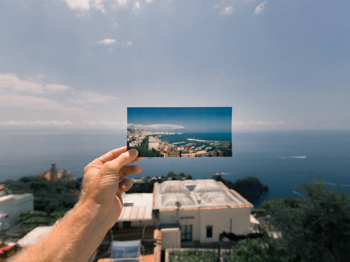 Eine Postkarte in einer Hand vor das fotografierte Motiv gehalten.