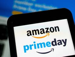 Das Amazon prime day Logo auf einem Smartphone vor einem Bildschirm, auf dem Amazon die Webseite geöffnet ist.