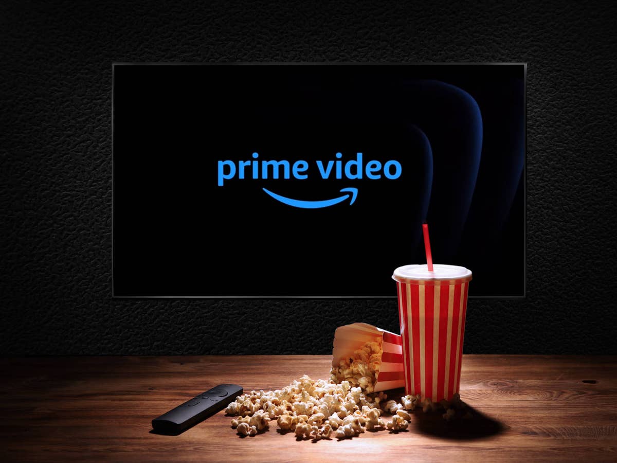 Logo von Prime Video auf einem Fernseher. Davor stehen Popcorn und ein Erfrischungsgetränk auf einem Holztisch.