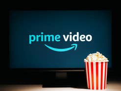 Logo von Prime Video auf einem Fernseher mit davor stehender Tüte Popcorn.