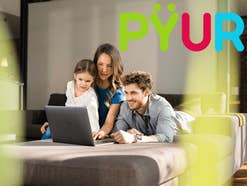 Drei Personen sitzen vor einem Laptop in einem modernen Wohnzimmer.