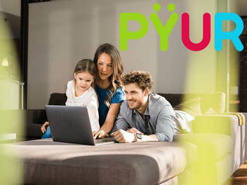 Drei Personen sitzen vor einem Laptop in einem modernen Wohnzimmer.