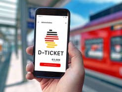 App mit Deutschlandticket auf Smartphone vor einem DB-Zug im Hintergrund