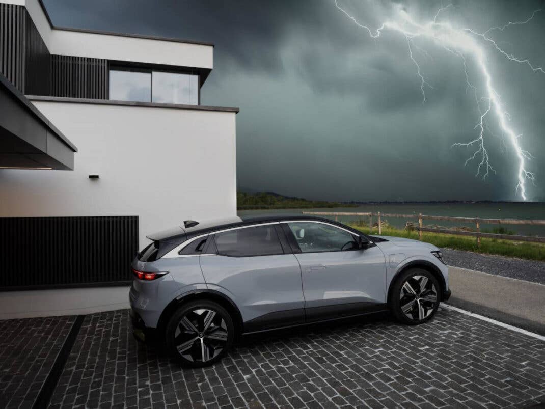 Renault Mégane E-Tech Electric steht vor einem Haus und im Hintergrund ist ein Blitz zu sehen.