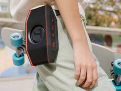 Eine Person, die unter einem Arm ein Skatenoard hat und an deren Hose ein Bluetooth Lautsprecher von Teufel hängt