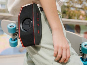 Eine Person, die unter einem Arm ein Skatenoard hat und an deren Hose ein Bluetooth Lautsprecher von Teufel hängt