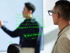 Ein Mann trägt die schwarzen Rokid Glasses und betrachtet eine Präsentation, während grüne Texteinblendungen und eine Audio-Wellenform in seinem Sichtfeld schweben.