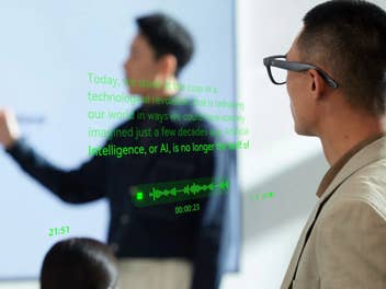 Ein Mann trägt die schwarzen Rokid Glasses und betrachtet eine Präsentation, während grüne Texteinblendungen und eine Audio-Wellenform in seinem Sichtfeld schweben.