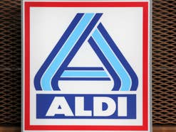 Aldi Logo vor einem verrosteten Gitter.