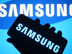 Samsung Logo auf einem Smartphone vor einem Samsung Logo im Hintergrund.