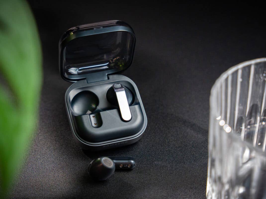 Die Samsung Galaxy Buds4 in der geöffneten Ladeschale. Ein Kopfhörer liegt draußen.