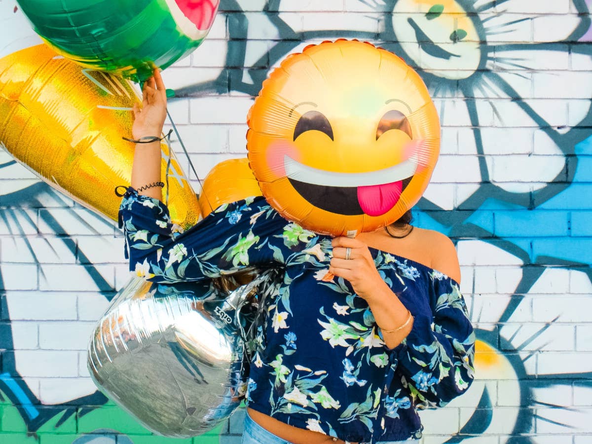 Eine Person hält einen Emoji-Ballon vor ihr Gesicht, in der Hand weitere Ballons