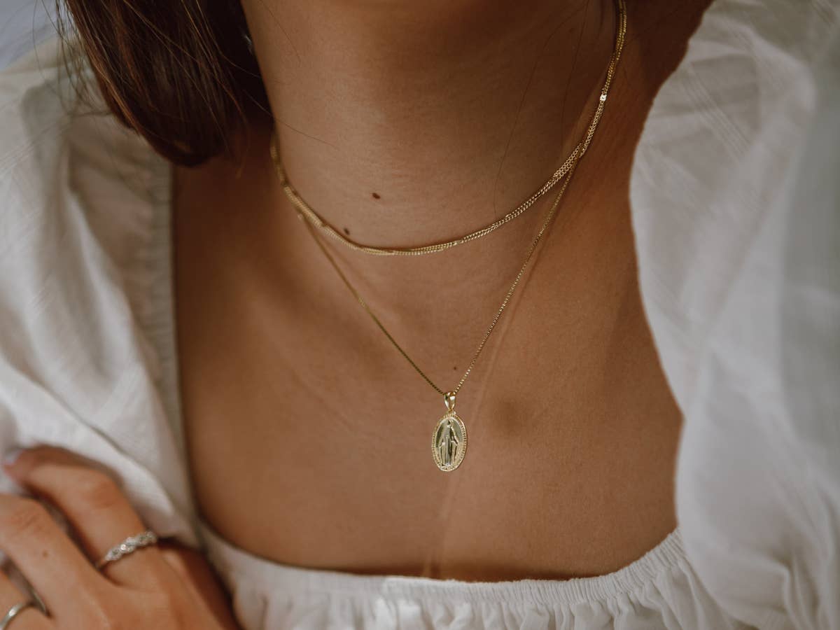 Schmuck Valentinstag Goldene Ketten um den Hals einer Frau in weißem Oberteil.