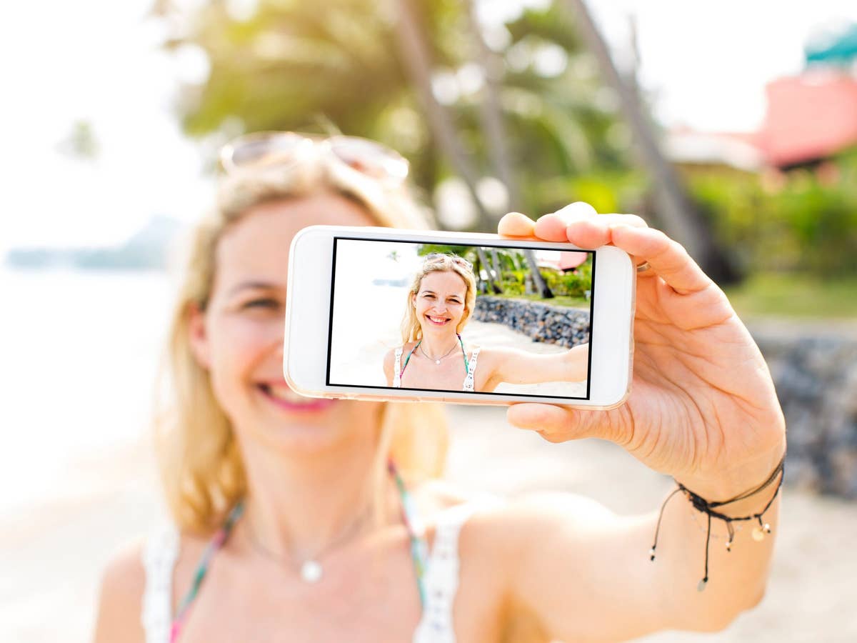 Gute Selfies zu machen, ist offenbahr vielen Smartphone-Nutzern besonders wichtig. Eine Frau am Strand macht ein Selfie mit ihrem Handy