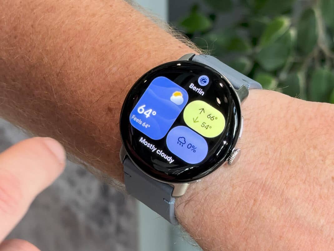 Nahaufnahme einer Google Pixel Watch 4, die Wetterinformationen für Berlin anzeigt, 64°F und überwiegend bewölkt.