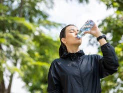 Mulher bebendo água depois de treinar na cidade ao nascer do sol. Jovem asiático bebendo água depois de correr ao ar livre. Conceito de estilo de vida saudável e ativo.