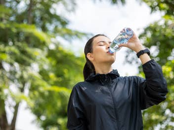 Mulher bebendo água depois de treinar na cidade ao nascer do sol. Jovem asiático bebendo água depois de correr ao ar livre. Conceito de estilo de vida saudável e ativo.