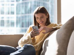 simyo mit Neustart: Das bietet der Discounter heute Eine Frau sitzt mit dem Handy auf der Couch