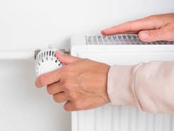 Eine Frau dreht am Thermostat einer Heizung.