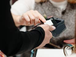 Eine Person hält seine Bankkarte an ein Kartenlesegerät, dabei greift die Kassiererin nach der Karte.