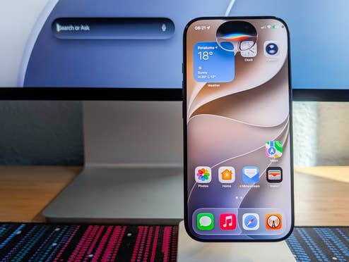 iOS 27 im Foldable-Format über iPhone Mirroring Neue Siri-Oberfläche auf einem iPhone vor einem Mac mit schwebendem Siri-Suchfeld