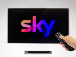 Sky-Logo auf einem Fernseher, der von einer Frau mit einer Fernbedienung eingeschaltet wird.