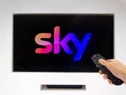 Sky Logo auf einem Fernseher, Hand schaltet TV über Fernbedienung ein.