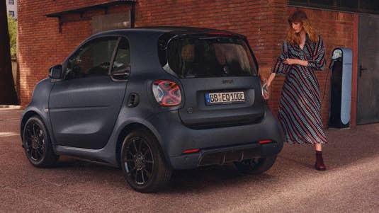 Eine Frau schließt den Smart EQ fortwo edition bluedawn an eine Ladesäule an