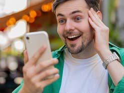 Mann mit Smartphone in der Hand freut sich.