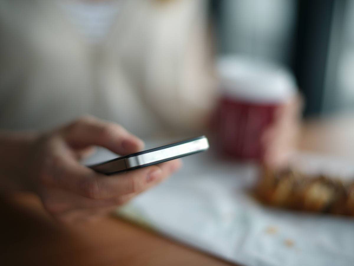 Smartphone in der Hand einer Person beim Frühstück.