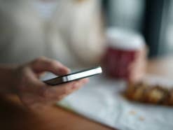 Smartphone in der Hand einer Person beim Frühstück.