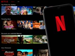 Smartphone mit Netflix-Logo dahinter ein Blick auf verschiedene Serien und Filme bei Netflix