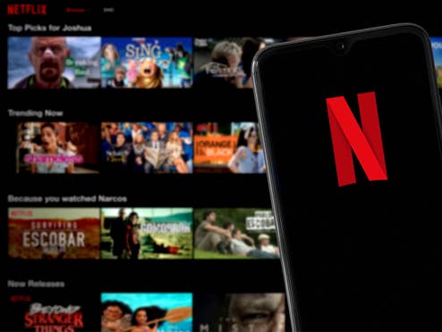 Smartphone mit Netflix-Logo dahinter ein Blick auf verschiedene Serien und Filme bei Netflix