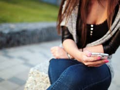 Eine Frau sitzt auf einem Stein und liest eine SMS