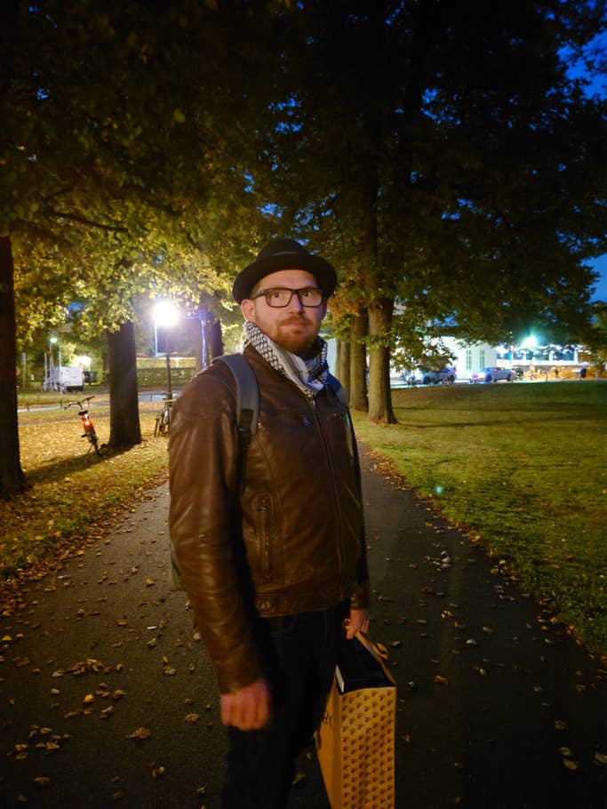 Ein Mann in einer Allee bei Dämmerung und im Schein von Straßenlaternen.