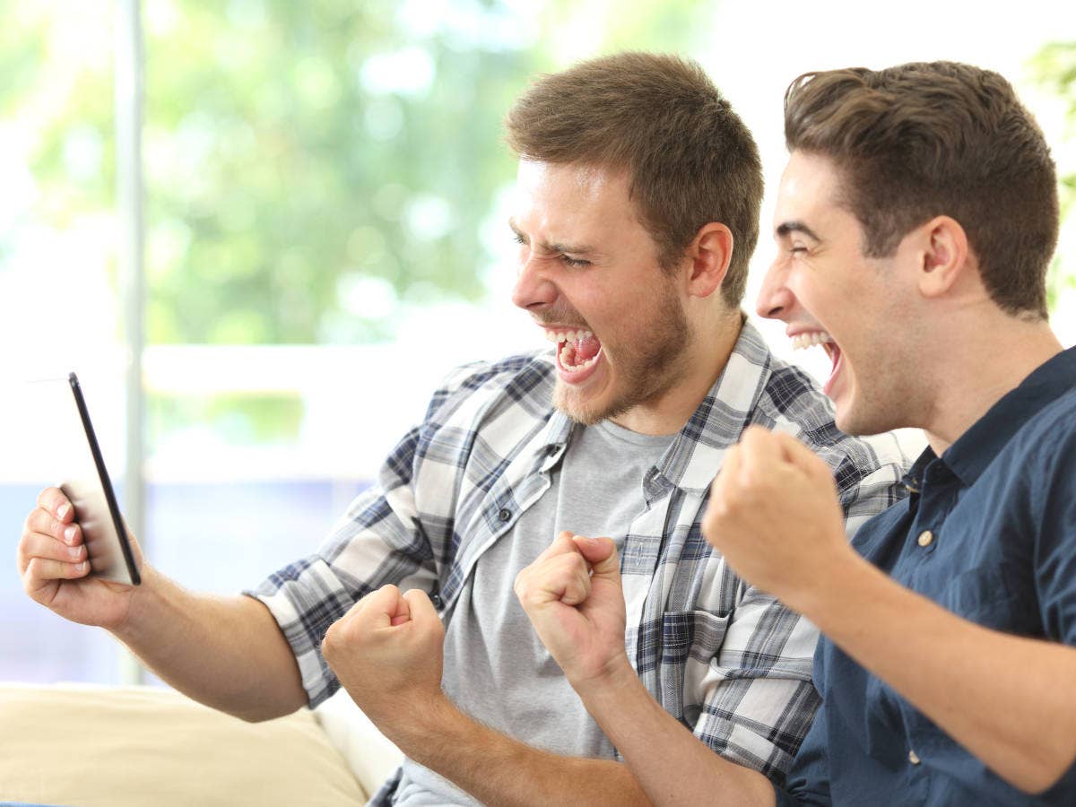 Zwei Männer schauen Sport auf einem Tablet PC und jubeln.