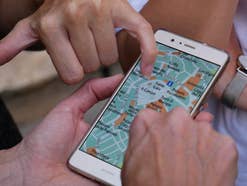 Stadtplan auf einem Handy Mehrere Hände zeigen auf eine Navi-App auf einem Handy