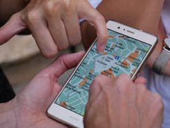 Mehrere Hände zeigen auf eine Navi-App auf einem Handy