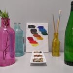 Tisch mit Flaschen, Farben auf einer Leinwand und Münzen in einer Schale