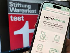 Amazon Renewed Webseite auf einem Smartphone mit Logo der Stiftung Warentest im Hintergrund.