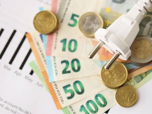 strompreis-bei-minus-480-euro-welche-haushalte-fuers-stromverbrauchen-jetzt-geld-bekommen Euroscheine und Münzen unter einem Stromkabel mit EU-Stecker