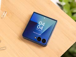 Ein Samsung Galaxy Z Flip7 Smartphone auf einer Holzoberfläche, das die Uhrzeit und das Datum zeigt.