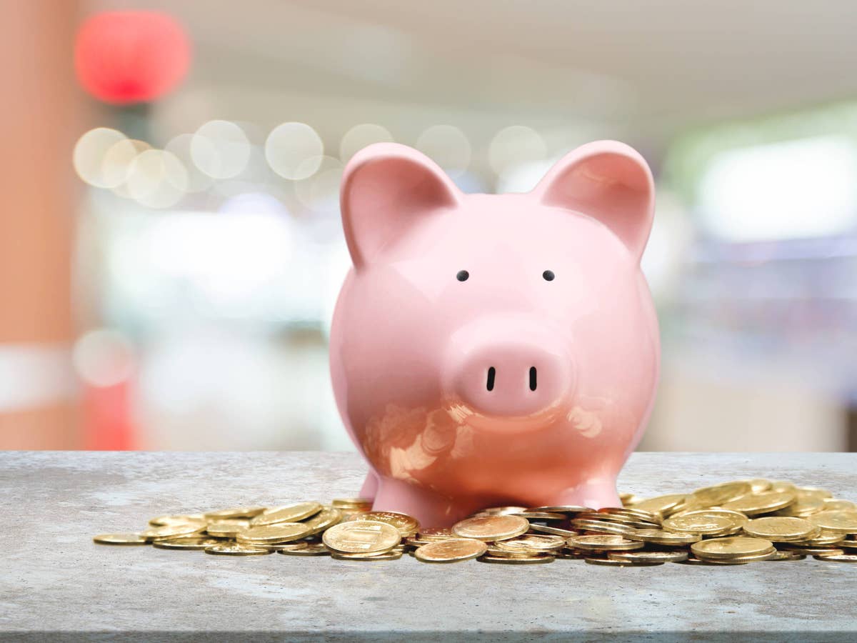 Sparschwein steht vor Goldmünzen.